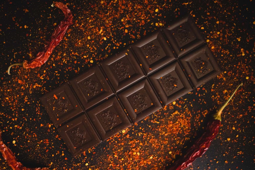 An image of a chocolate bar surrounded by chili powder and a few chili peppers. 